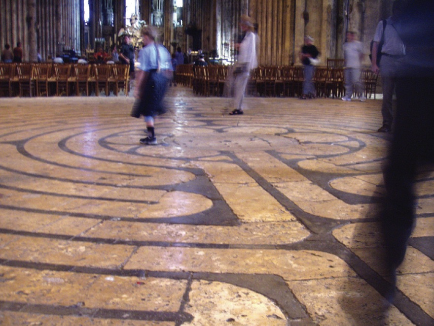 Photo of labyrinth on the floor of a cathedral with woman walking through it.