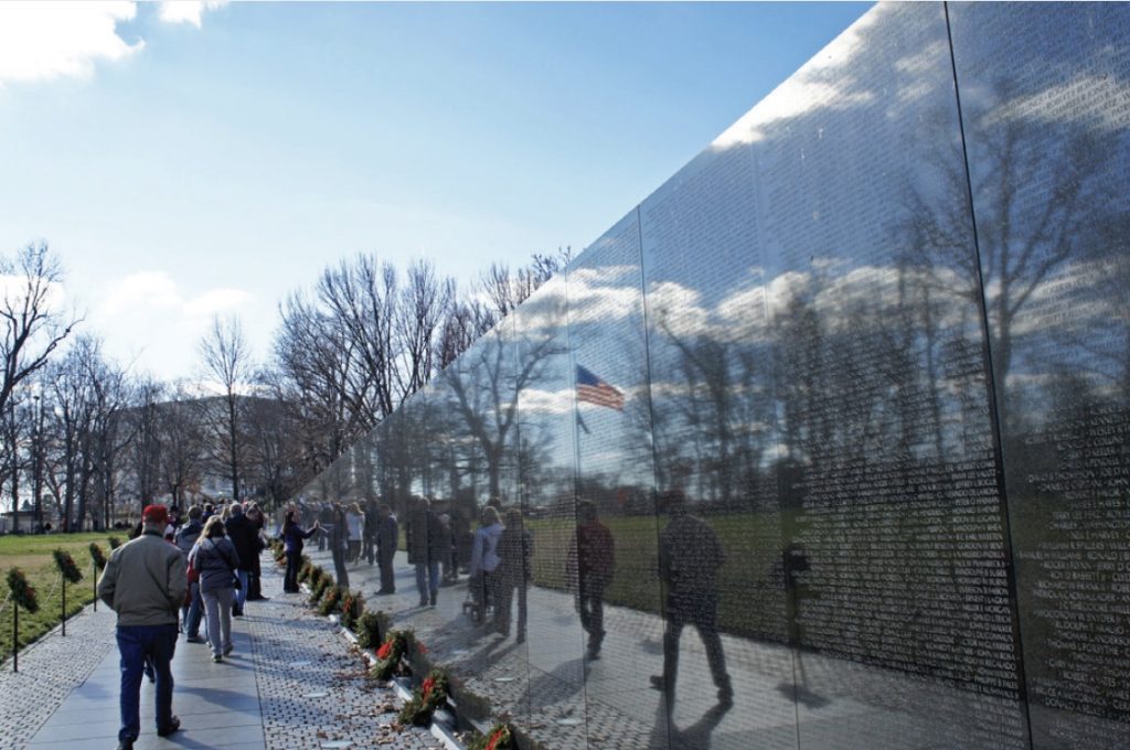 Photo of people viewing black reflective wall that is Vietnam War Memorial in Washington DC.