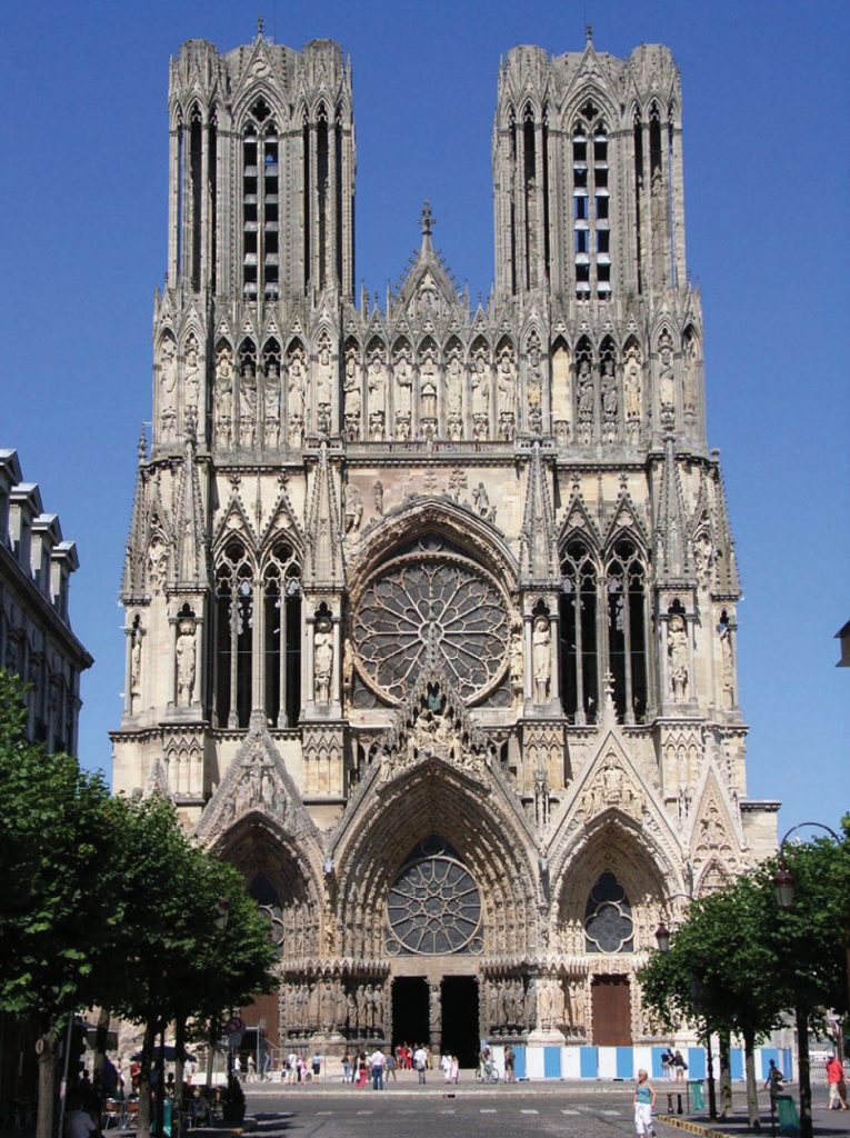 Photo of Reims Cathedral in France, with high Gothic facade, lavish scupltural deorations, and long, tall windows