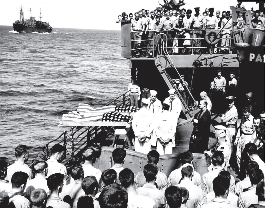 Photo of soldiers on a naval warship surrounding bodies and preparing to throw them overboard for burial at sea.