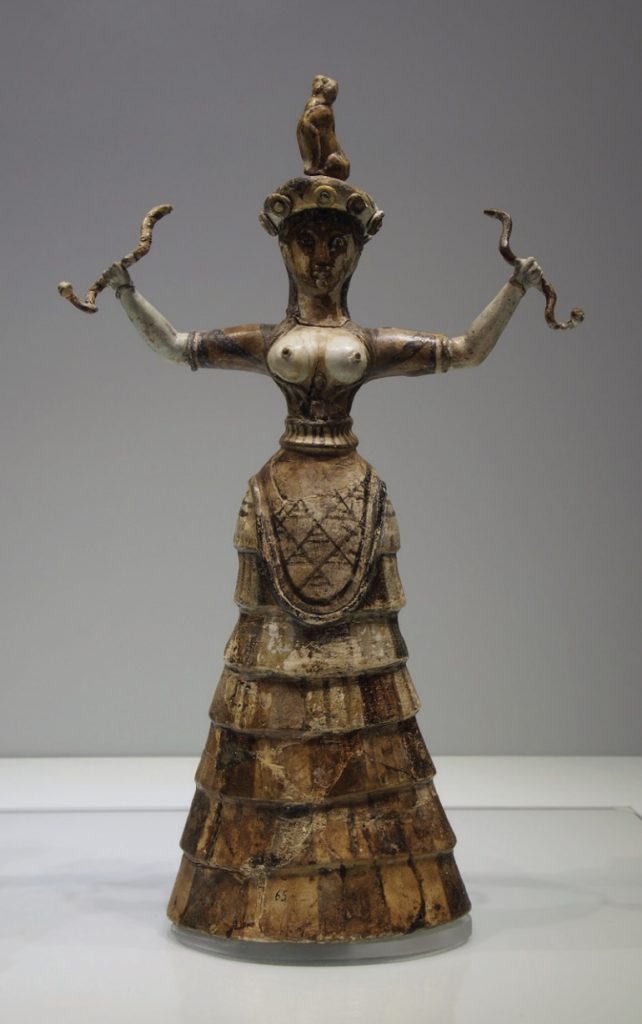 Photo of small statue or relic of a snake goddess, holding a snake in each upraised hand.
