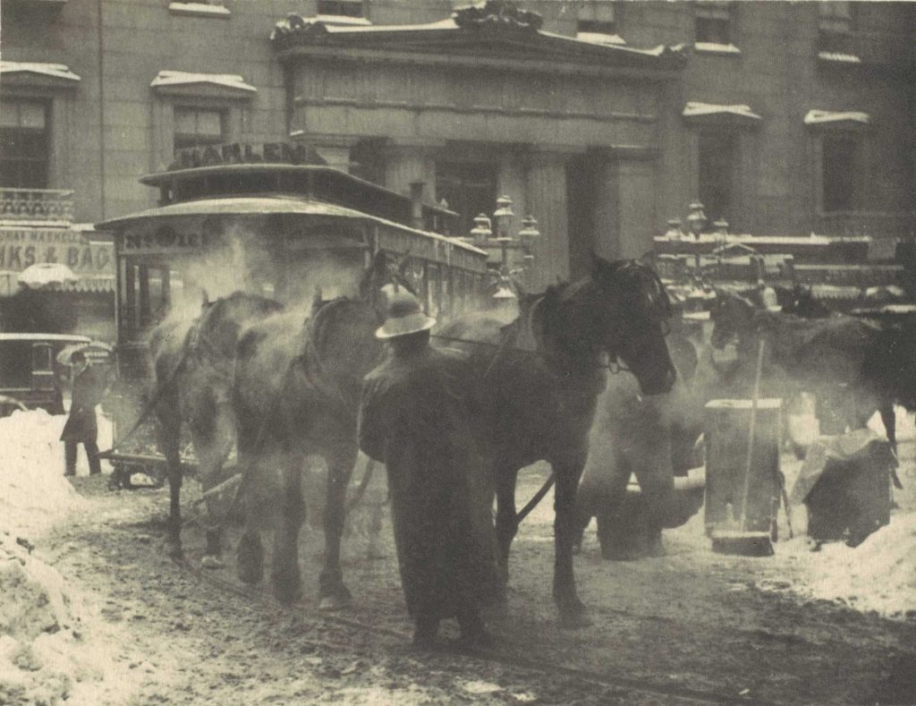 Image of The Terminal by Alfred Stieglitz. Shown is a busy roadway with a man infront of two horses and a trolly in the background. Photogravure.