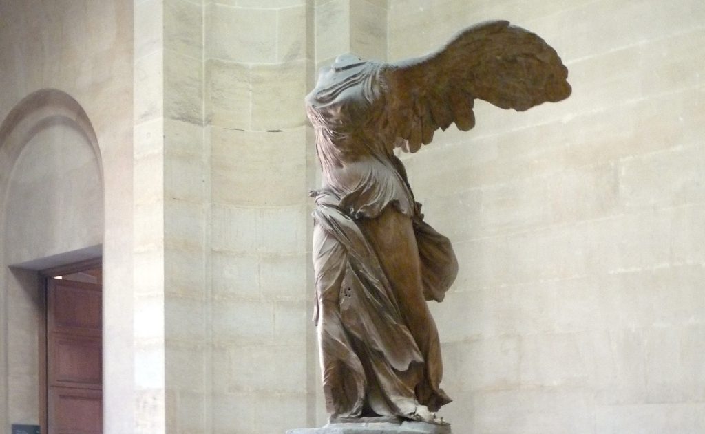 Image of The Winged Victory Nike of Samothrace. Marble statue shown with grand wings and elaborate draping across the goddesses' body, missing her head.
