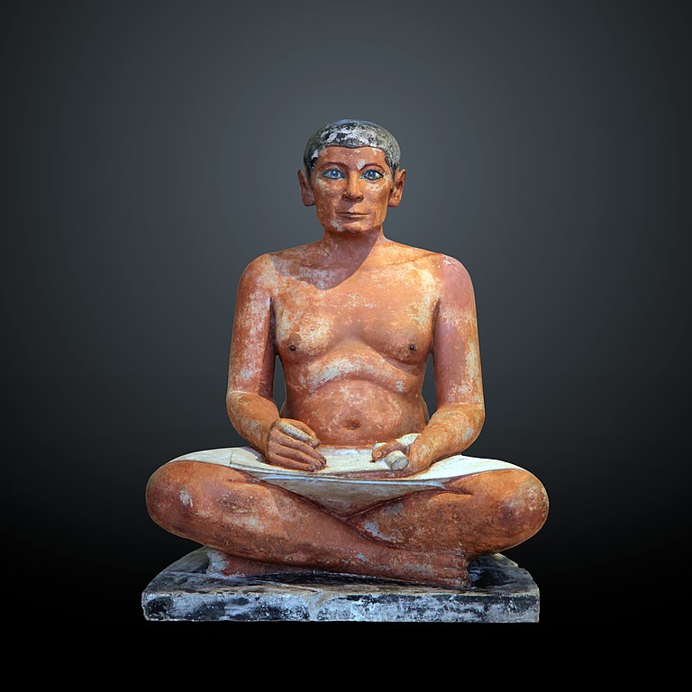 Frontal view of the Seated Scribe, shown sitting cross legged holding papyrus.