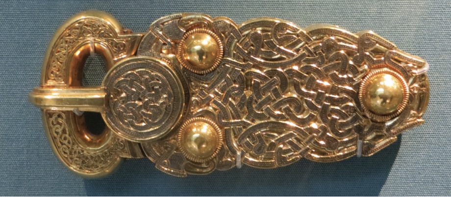 Photo of gold colored belt buckle with detailed designs.