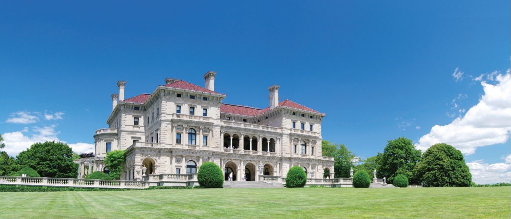 Photo of large stone mansion with 3 storeis and red roof top, large expansive lawn.