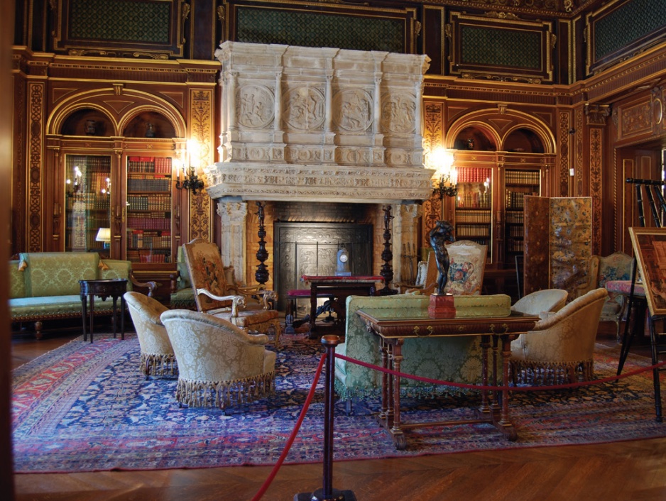Photo of a library with seating and large fireplace at center, books inset in wooden walls.