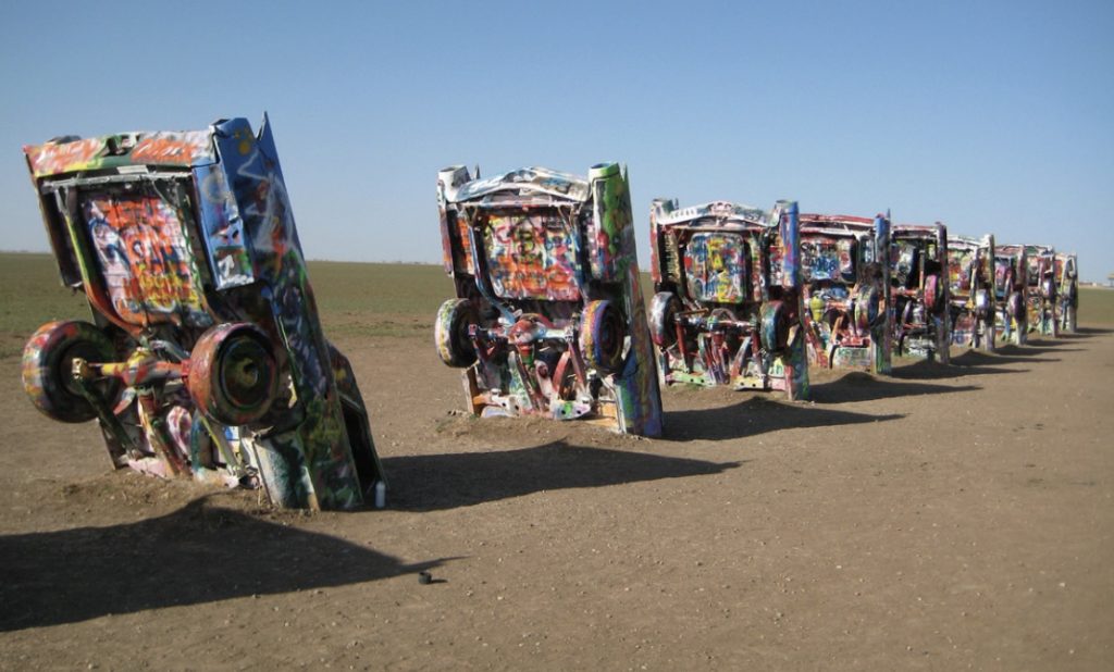 Photo of several brightly colored cars with front ends buried in the Earth.