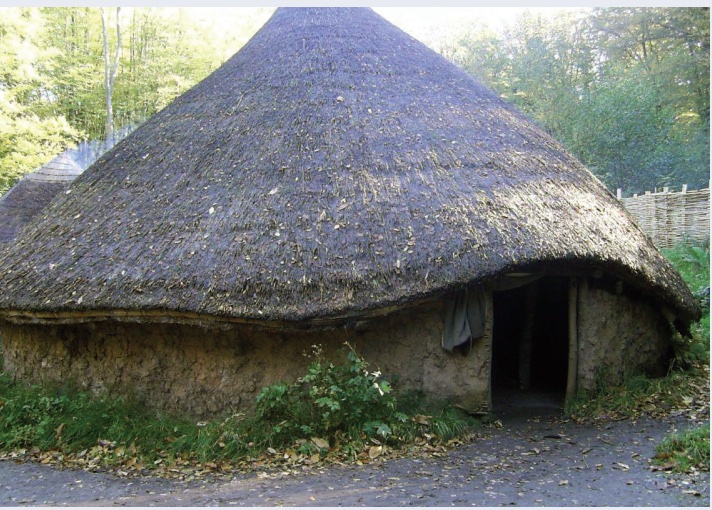 Photo of round house with pointed top made of sticks, mud, rammed earth.