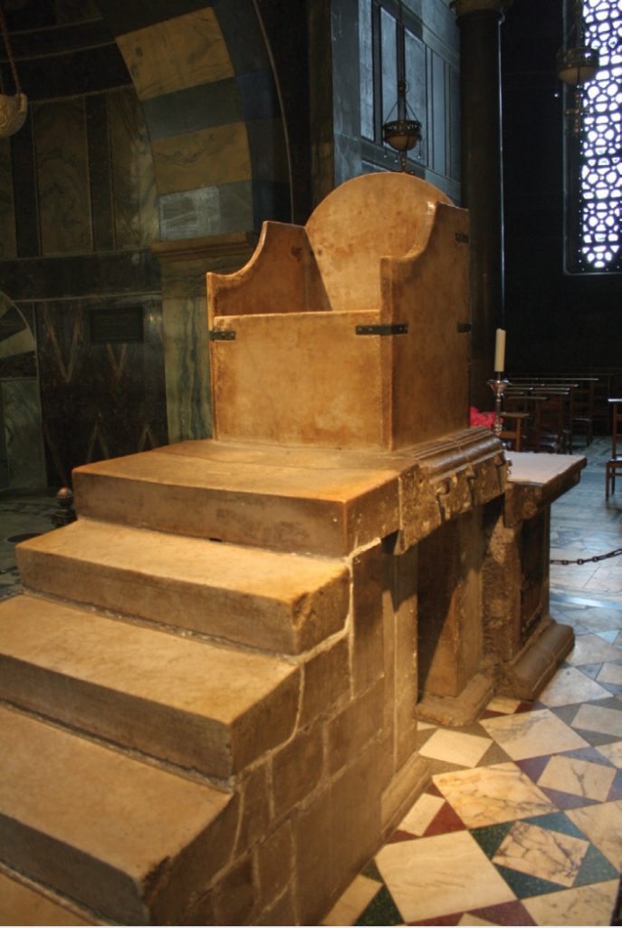 Photo of a wooden throne atop a small set of stairs.