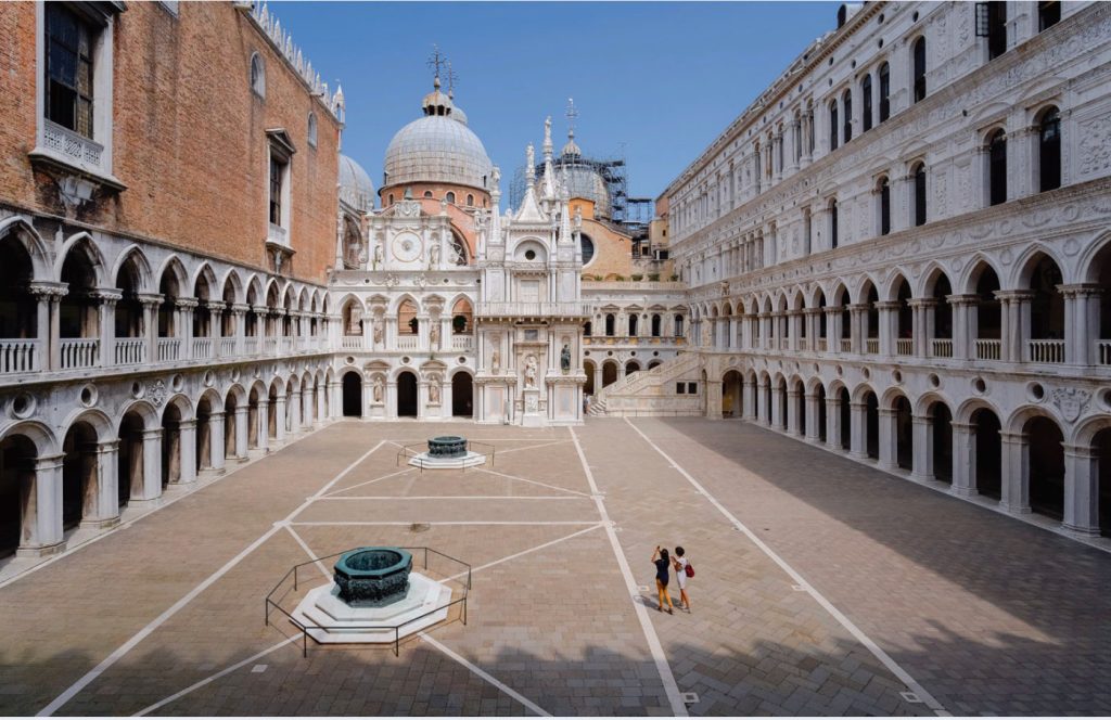 Photo of a courtyard with concrete flooring and surrounded by high walls with arched windows or portals.