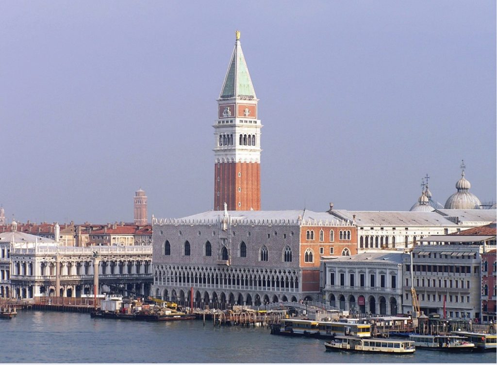 Photo of a tall tower with copper-green pointed top among city and coastal landscape.