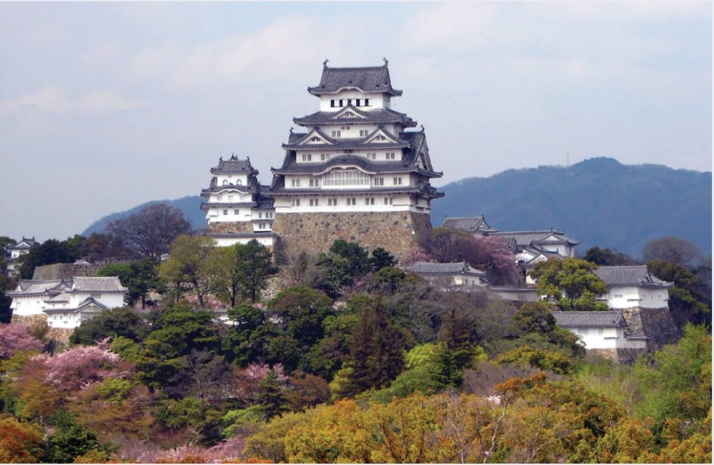 Photo of a Japanese castle atop a stone foundation at top of hill.
