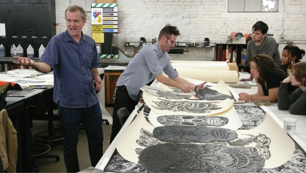 Photo of several artists working at table on linoleum prints.