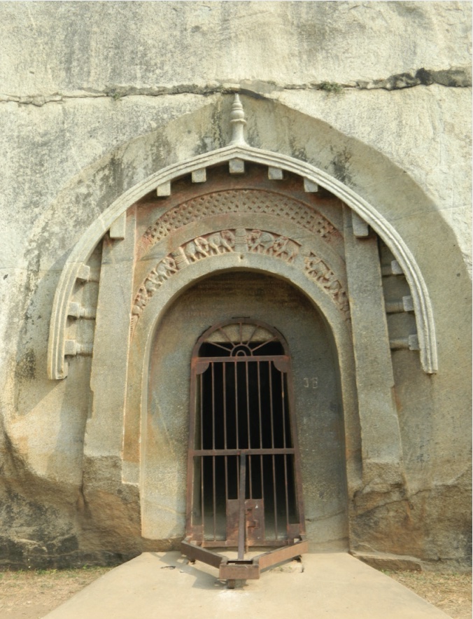 Photo of gated entrance to cave in rock wall with ornate carvings around door.
