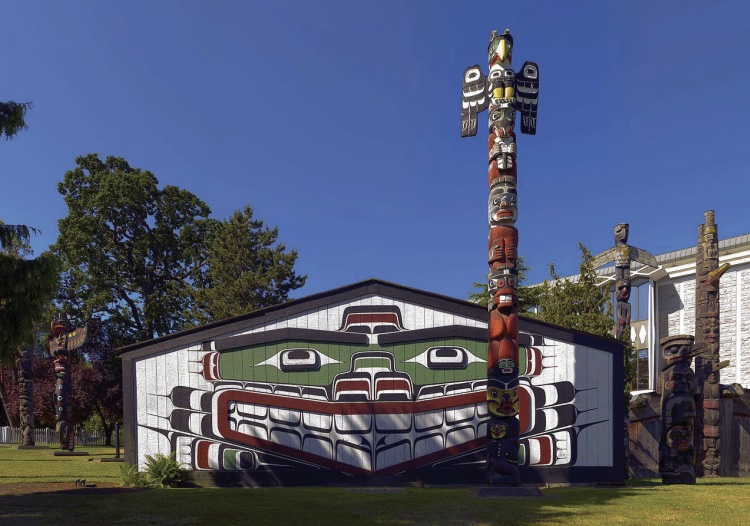Photo of a white house with colorful painting of chief and totem pole in front.