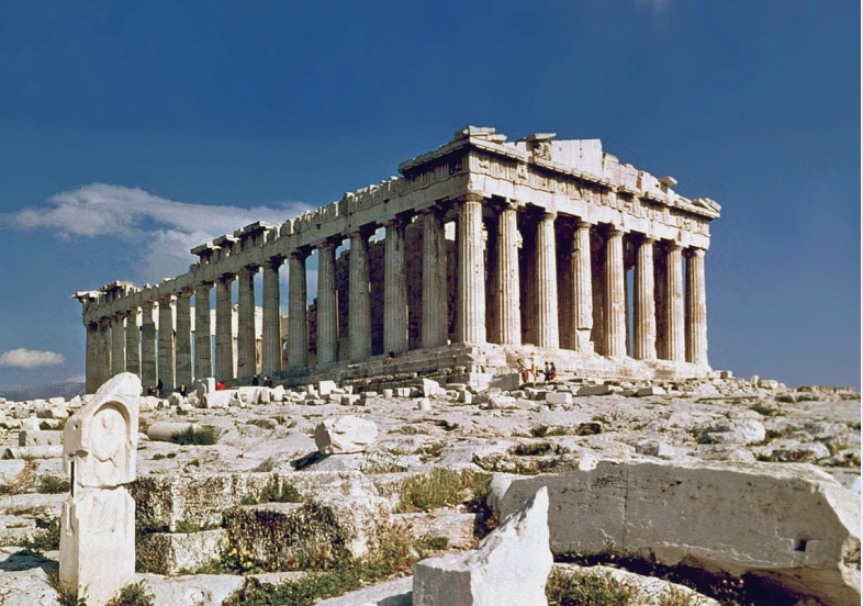 Photo of a crumbling temple (Parthenon) with large columns around perimeter, set among rocky landscape.