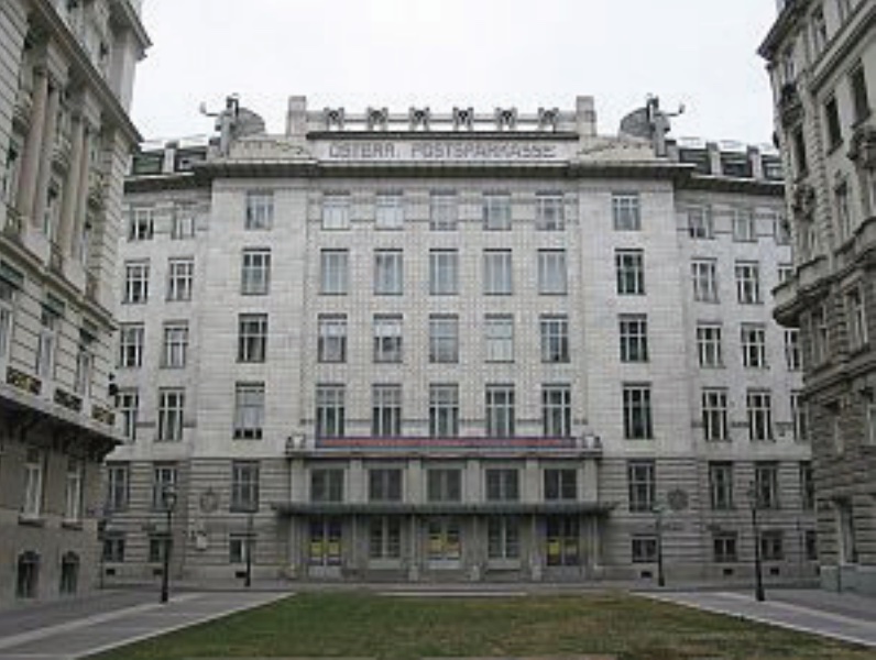 Photo of facade of large grey building with several floors and lots of windows facing grassy courtyard.