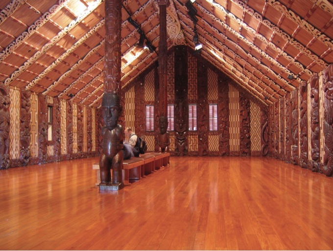 Photo of inside of a meeting house depecting a large open hall and columns in middle with wooden carvings.