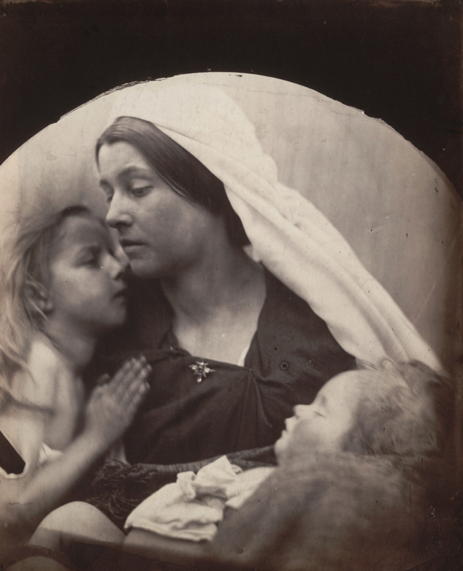 Image of Madonna with Children by Julia Margaret Cameron. Woman as Madonna with a child to her left and she holds a sleeping child in her arms.