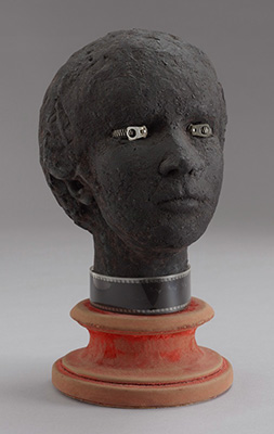 Image of Specter of the Gardenia by Marcel Jean. Plaster head with painted black cloth, zippers in the place of eyes with a strip of film on the neck. It sits atop a velvet covered wood base.