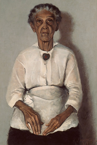 Portrait of an elderly african american woman seated with her hands in her lap. Her hair is braided and pulled back and she wears a heart brooch, and an apron.
