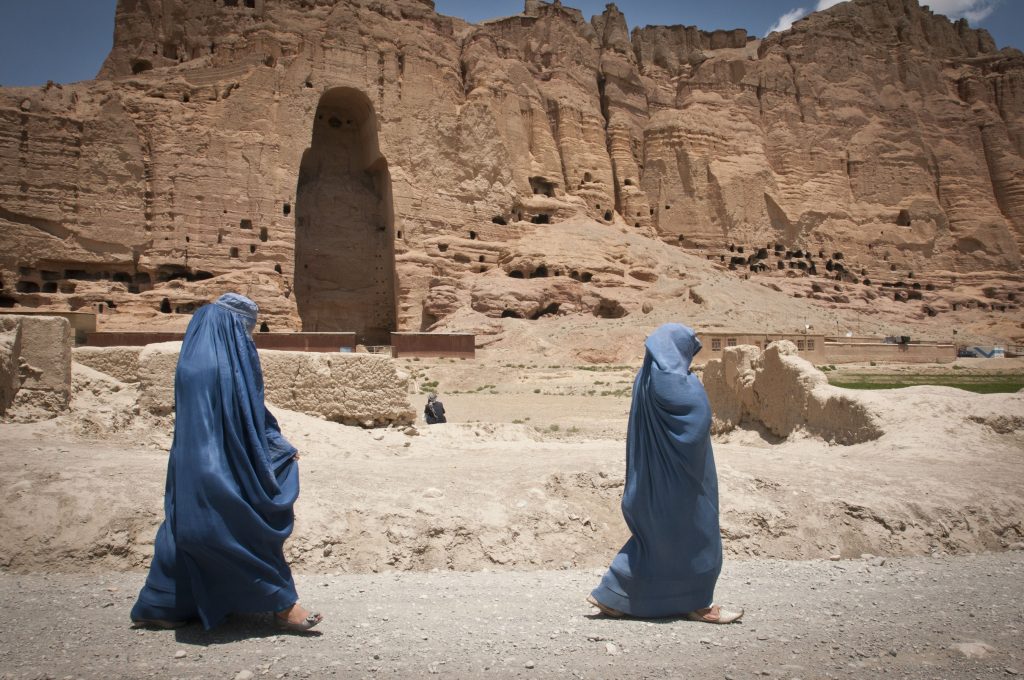 Women in burkas walk past one of the empty caves where a Bamiyan Buddha statue stood.