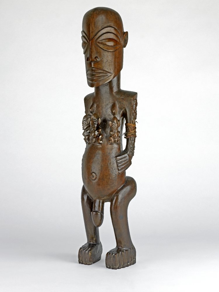 Image of a carved nude male wood figure with smaller men carved on his chest.