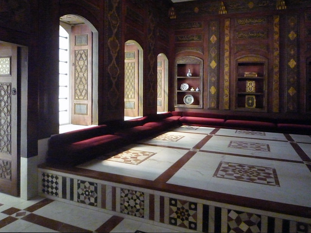 Image of the Damascus Room. Walls made of wood with reliefs, covered in gold leaf. The floor is a of colorful tiles and in the center a small fountain comes up.