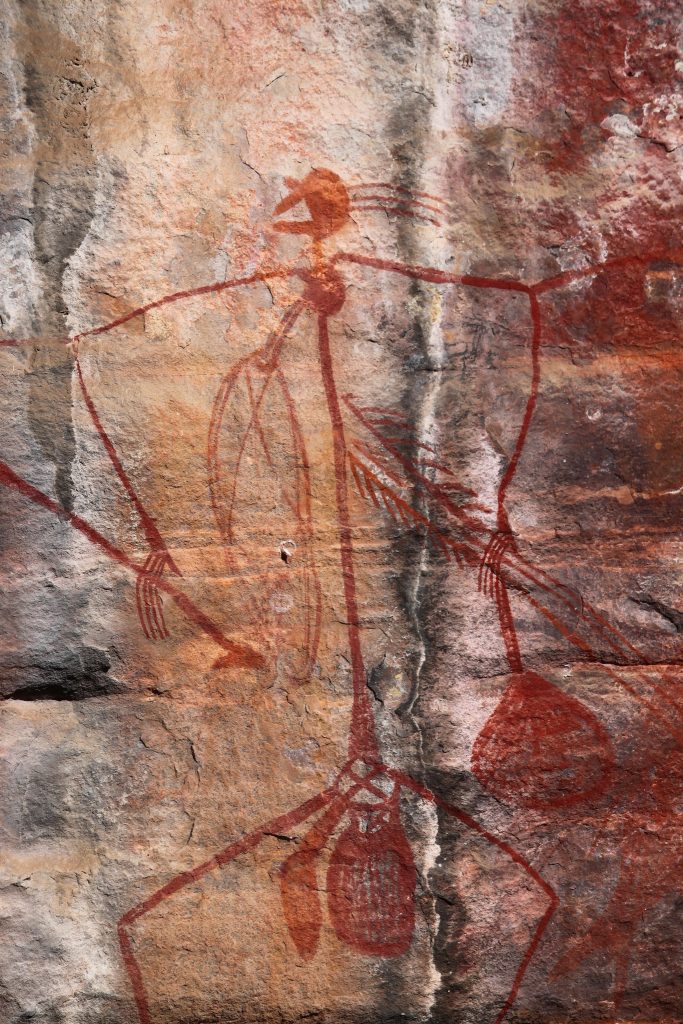 Image of Aboriginal Rock Art at Ubirr Art Site in Kakadu National Park, Australia. Depicted is a long stick-like figure, holding objects in both hands.