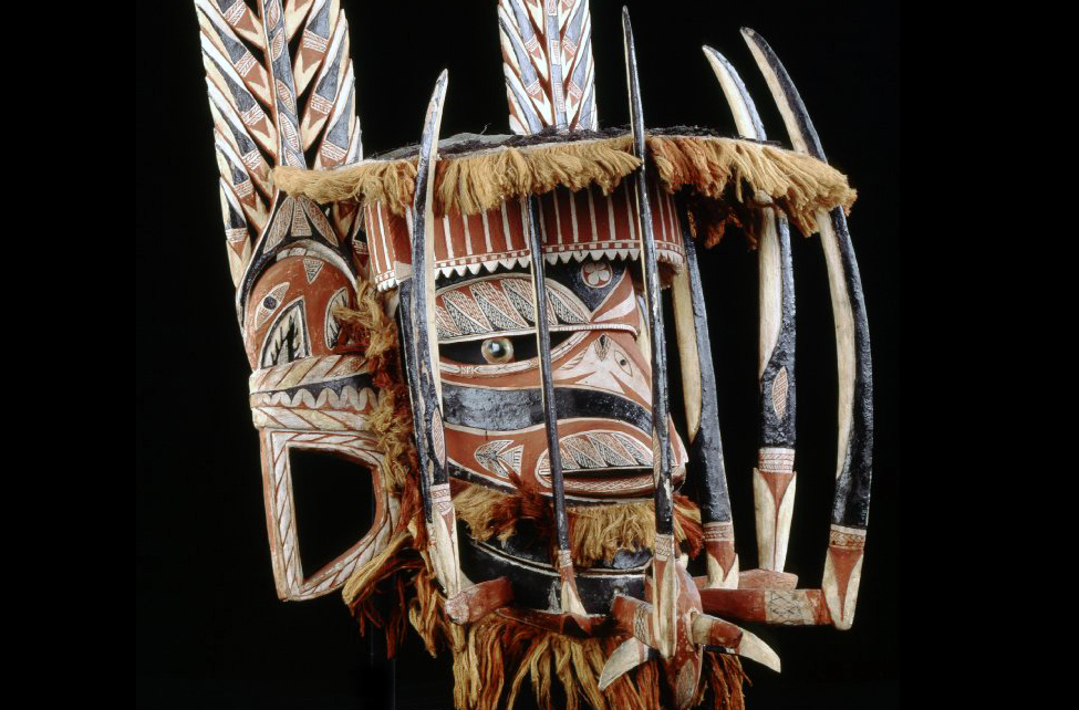 A mask with a birdlike face and feather like pieces at the back. In the front is a row of spikes.