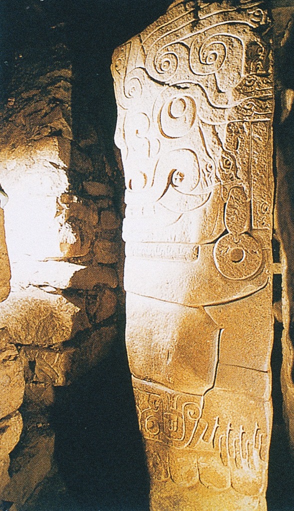 A stone monolith with swirled carvings in an underground chamber.
