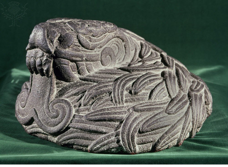 A stone sculpture showing a serpent with exaggerated fangs and tongue, and elaborately carved feathers.