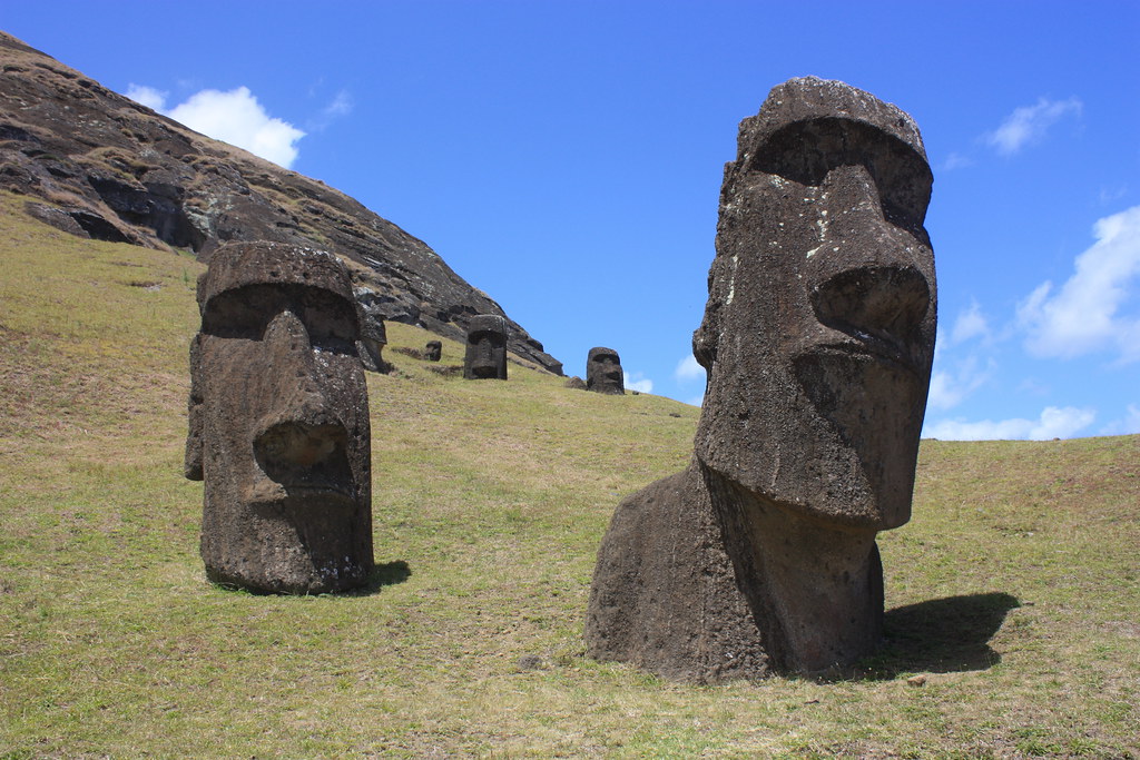Close up details of 2 of the moai standing on a hill where only the head and some shoulders can be seen.