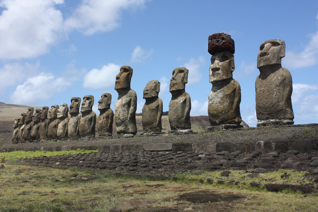 A row of 15 excavated statues standing on a platform. one has an additional stone on its head.