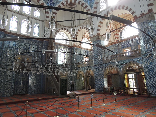 A larger room with striped arches, tiled floors and a chandelier made of concentric circles of lights.