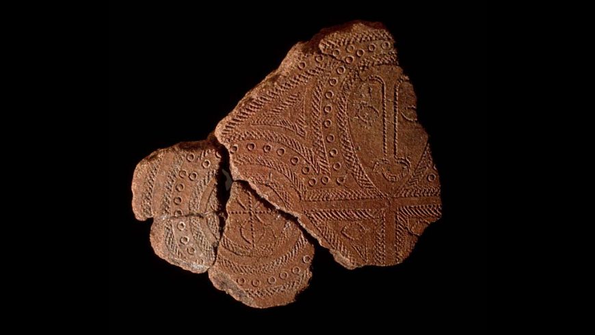 Image of terra cotta pottery fragments with inticate carved details on them in circular patterns and a human form.