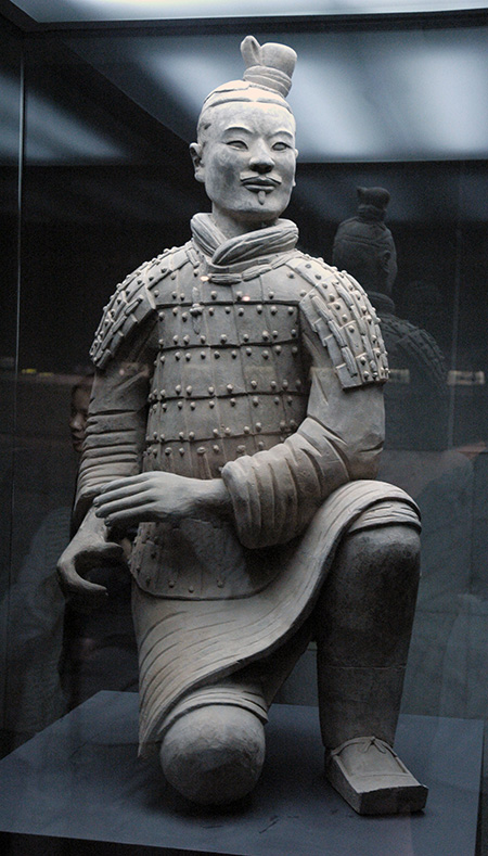 Terracotta warrior kneels within glass display at a museum.