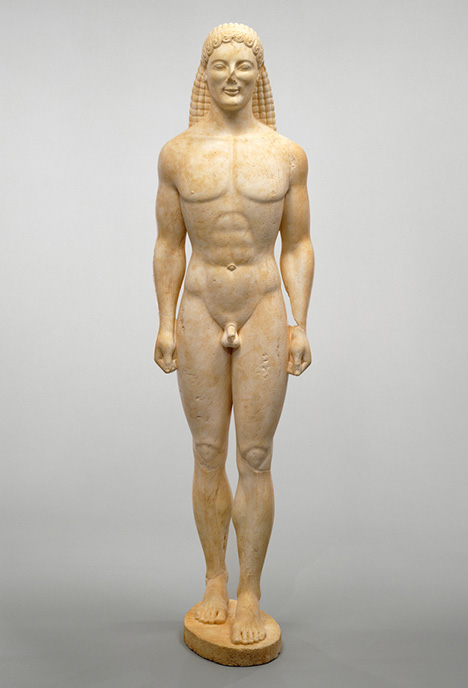 A statue of a nude male with long braided hair. His nose has been damaged over time.