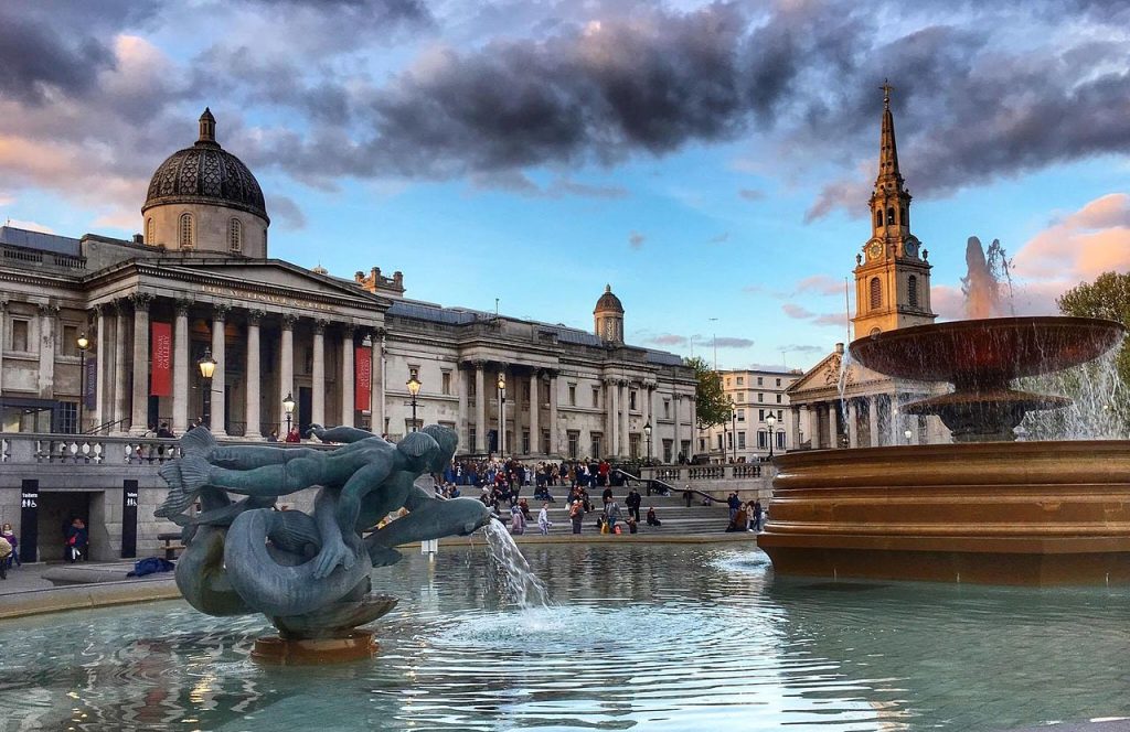 The front of the National Gallery building showing the fountain with a sculpture of mermaid-type people riding dolphins.