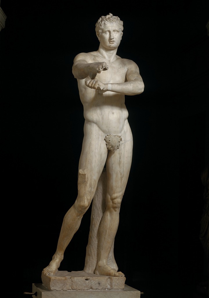A statue of a Roman man with arms extended, nude aside for a leaf covering.