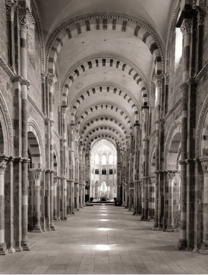 Black and white photo looking down a nave toward the apse of a cathedral, with arched doorways along length.
