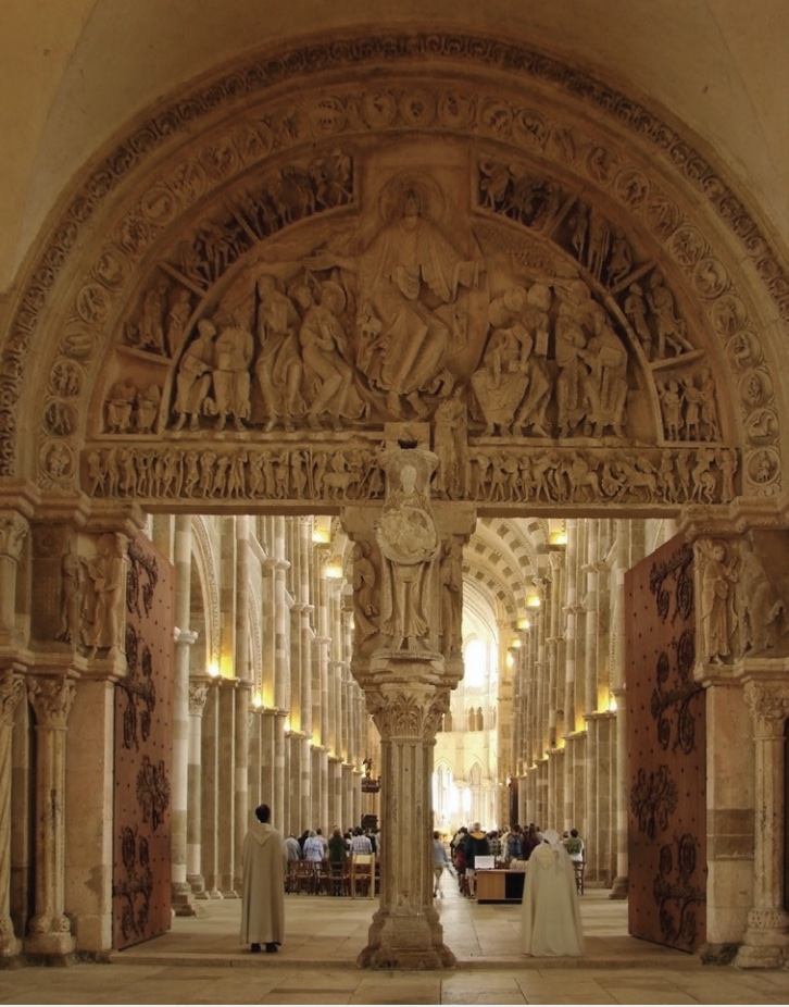 Photo of an ornately decorated central portal of an abbey with pews filled with congregants.
