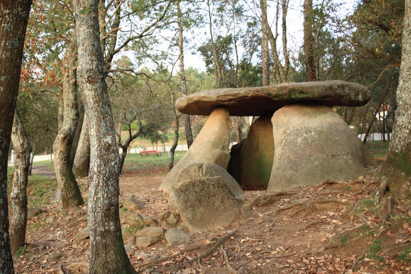 Photo of two megaliths supporting a horizontal stone among the trees.