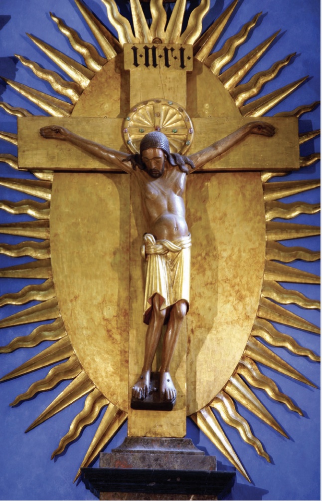 Photo showing crucifix with Christ on cross and sun-like design behind cross.