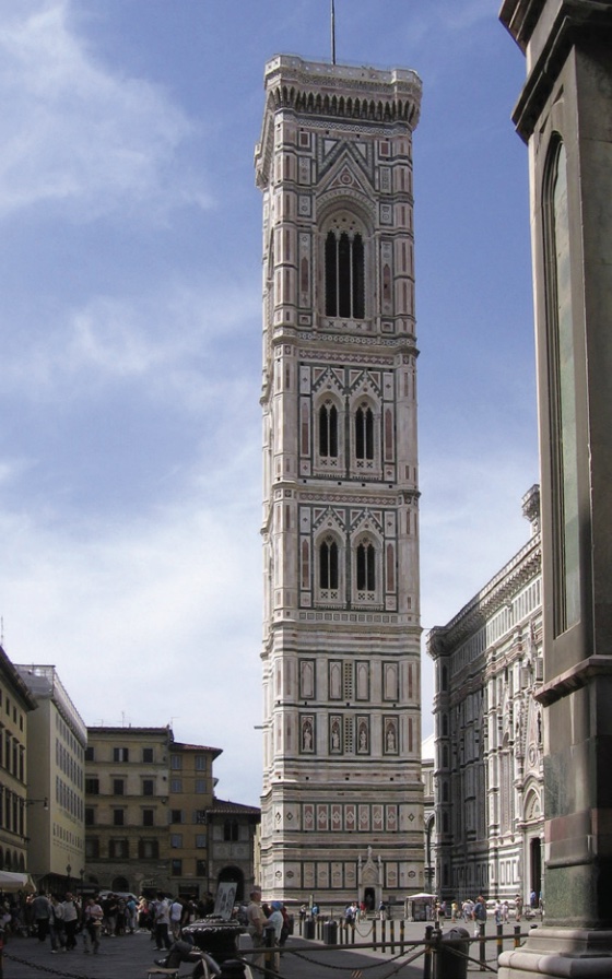Photo of a grey square-sided tall bell tower set amongst city buildings.