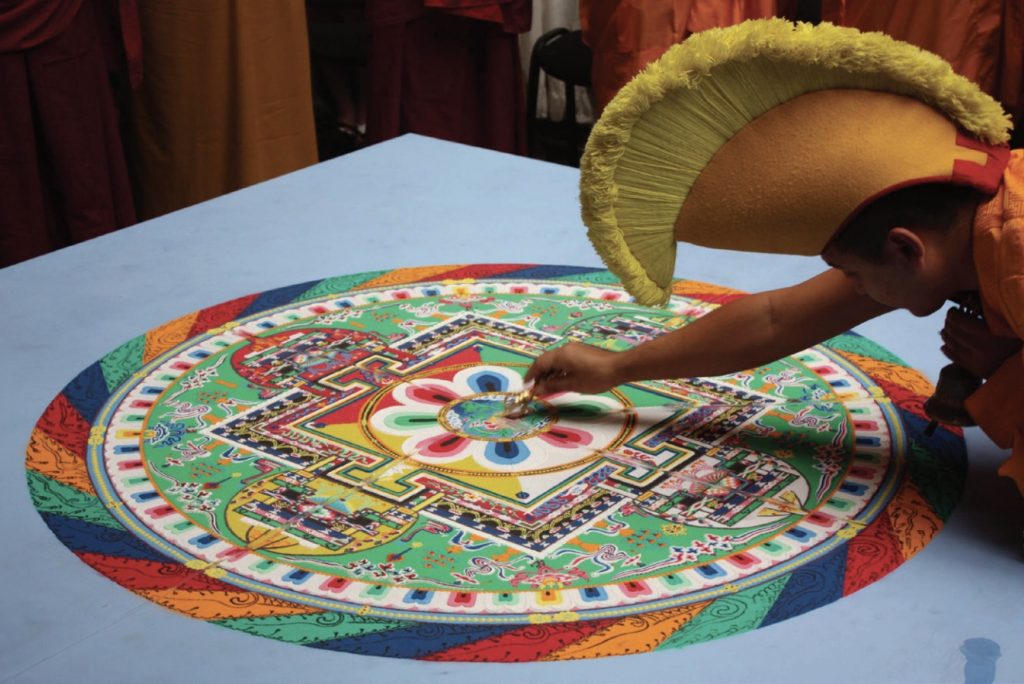 Photo of a sand mandala in many colors being created by a Tebetan Buddhist monk.