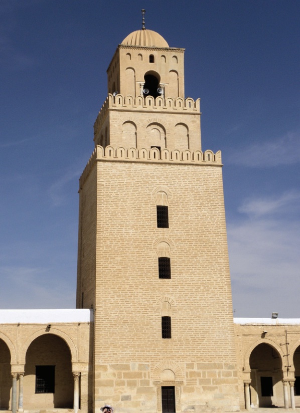 Photo of a tan-colored minaret against blue sky.