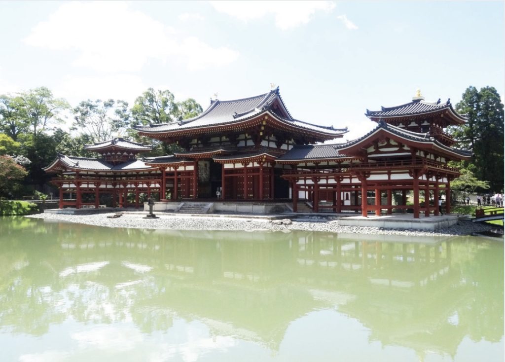 Photo of a large red pagoda and green pond in foreground.