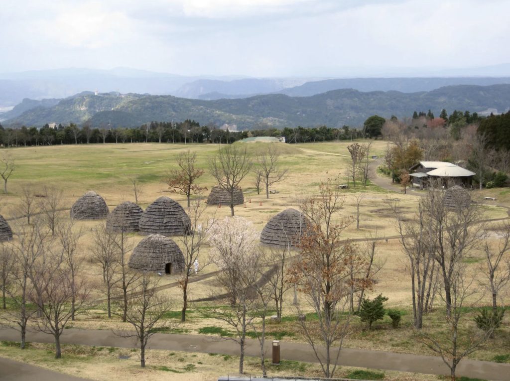 Photo of a settlement of huts among trees and grassy meadow.